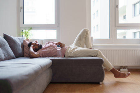 Young man lying on sofa after home workout, meditation at home, morning or evening workout routine.の写真素材