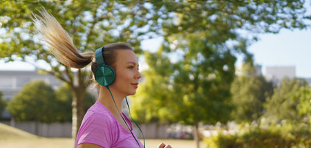 Young woman running outdoors, listening music. Exercising after work for good mental health, physical health, and relieving stress and boost mood. Banner with copy space.の写真素材