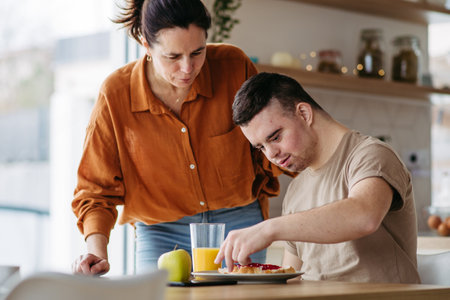 Young man with Down syndrome preparing breakfast with his mother at home. Morning routine for man...