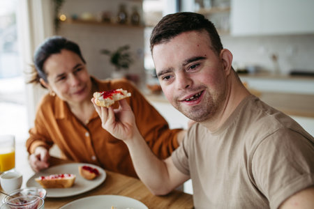 Young man with Down syndrome having breakfast with his mother at home. Morning routine for man with Down syndrome.の写真素材