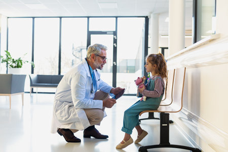 Friendly pediatrician talking to little patient. Cute preschool girl in greeting doctor in hospital corridor.の写真素材