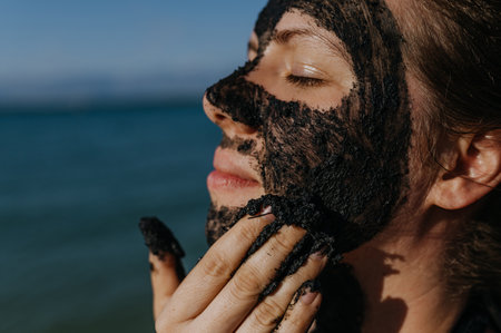 Woman applies healing mud to her face and body. Natural healing mud in Croatia on the beach.の写真素材