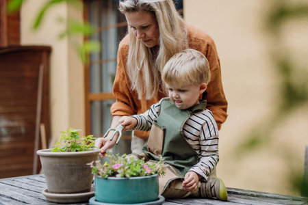 Mother and son taking care of plants in the garden, replanting, watering flowers. Mom and boy spending quality time together, bonding.の写真素材