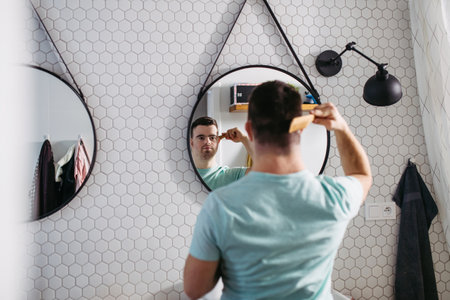 Young man with down syndrome in bathroom, combing his hairs.の写真素材