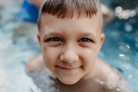 Little boy enjoying summer time in outdoor pool with his family, having fun.