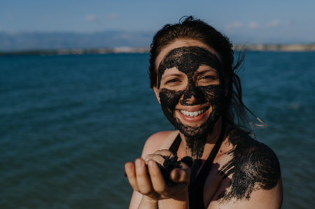 Woman applies healing mud to her face and body. Natural healing mud in Croatia on the beach.の写真素材