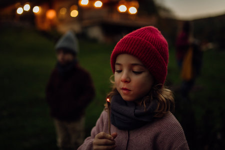 Portrait of cute girl blowing out flame on a burning stick. Family having a barbecue in the garden on an autumn evening.の写真素材