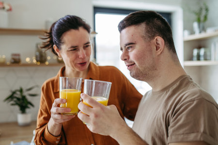 Portrait of young man with Down syndrome with his mother at home, toasting with juice. Morning routine for man with Down syndrome.の写真素材