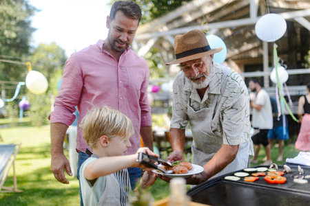 Father, grandfather and son grilling together at garden BBQ. Three generations of men at summer family garden party.の写真素材