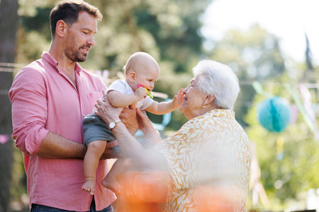 Great-grandmother holding little baby in her arms. Family summer garden party.