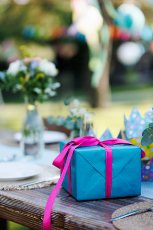 Close up of birthday gift in blue wrapping paper with pink ribbon. Summer garden birthday party in a beautiful garden.