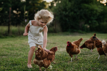 Little girl chasing chickens on a farm, running, having fun during the holidays at her grandparents countryside home.の写真素材