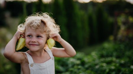 Girl holding green peppers as earrings. Caring for vegetable garden and growing, planting spring vegetables.の写真素材
