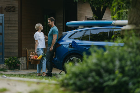 Couple standing by their electric car. Electric vehicle with charger in charging port.の写真素材