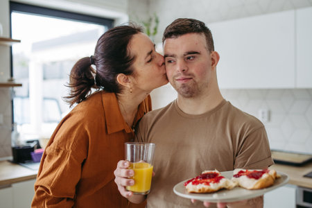 Young man with Down syndrome serving breakfast to his mother as a Mothers Day gift. Concept of...