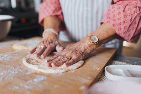 Close up of hands of senior woman preparing traditional easter meals for family, kneading dough for easter cross buns. Recreating family recipes, custom.の写真素材