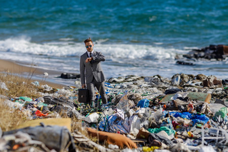 Businessman looking at watch, checking time standing on pile of waste on beach. Consumerism versus...