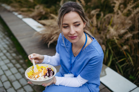 Nurse having healthy lunch in front of hospital building, taking break from work. Importance of breaks in healthcare.の写真素材
