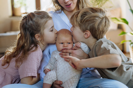Siblings kissing the cheeks of a little baby. Big brother and big sister meeting newborn sister, enjoying together time.の写真素材