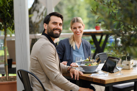Business lunch for two managers, discussing new business project. Couple sitting outdoors on terrace restaurant, having dinner date.の写真素材