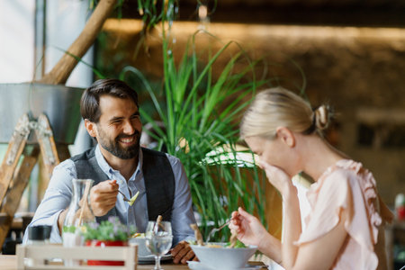 Happy loving couple at date in restaurant. Husband and wife sitting at table, laughing, having lunch in modern cafe.の写真素材