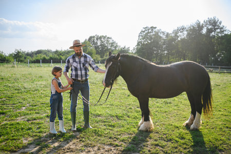 Father and young daughter taking care of a horse on a farm, leading it to the paddock. Concept of multigenerational farming.の写真素材