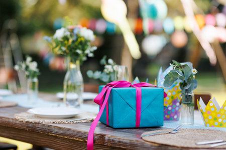 Close up of birthday gift in blue wrapping paper with pink ribbon. Summer garden birthday party in a beautiful garden.の写真素材