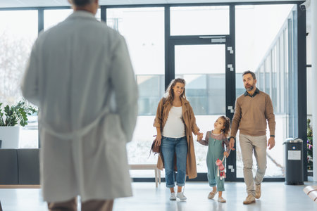 Girl patient looking forward to her doctor and examination in a modern clinic. Girl arriving in hospital with her parents. Emotional support during medical examination.の写真素材