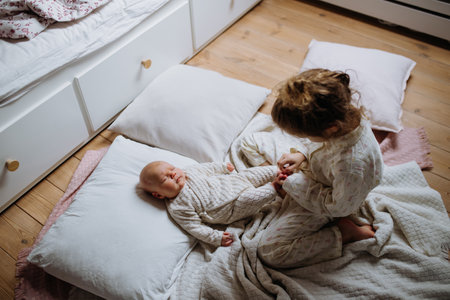Big sister playing with newborn, little baby. Girl looking at new sibling, holding babys small feet. Sisterly love, joy for new family member.の写真素材