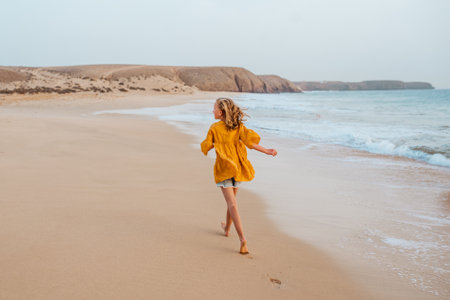 Young girl on beach. Rear view of blonde girl enjoying sandy beach, looking at crystalline sea in Canary Islands. Concept of beach summer vacation with kids.の写真素材