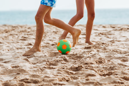 Siblings playing on beach with ball, playing football. Concept of family beach summer vacation with kids.の写真素材