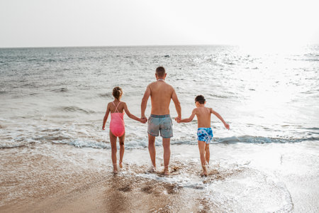 Father with two kids running on beach. Young family enjoying sandy beach, looking at crystalline sea in Canary Islands. Concept of beach summer vacation with kids.の写真素材