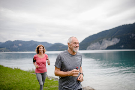 Senior couple running by lake in nature. Elderly husband and wife spending active vacation in the mountains, enjoying physical activity and relaxation outdoors.の写真素材