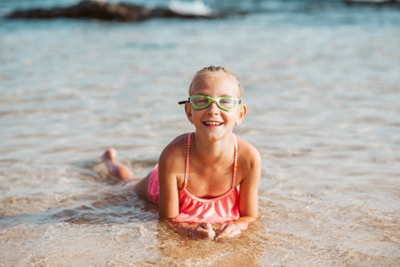 Young girl playing, swiming and splashing in fresh sea water. Smilling blonde girl in swimsuit with and swimming goggles. Concept of beach summer vacation with kids.の写真素材
