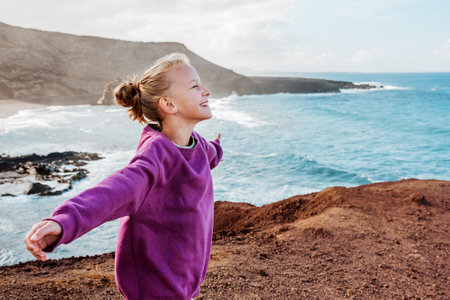 Young girl with closed eyes enjoing sea wind blowing in face. Smilling blonde girl enjoying nature of Canary islands. Concept of beach summer vacation with kids.の写真素材