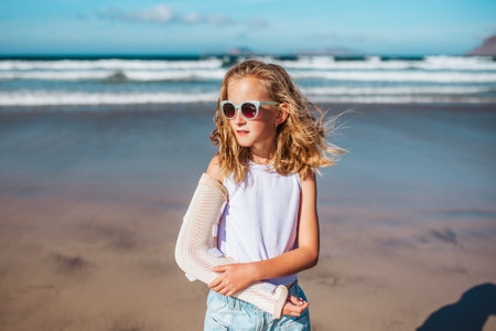 Girl with broken arm on beach. Young blonde girl has arm cast, injured during family vacation in holiday resort. Concept of beach summer vacation with kids.の写真素材