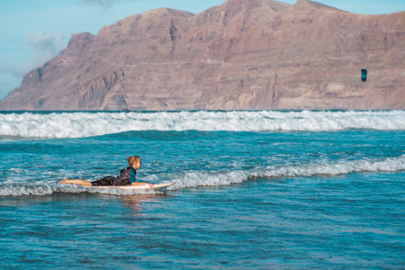 Young boy surfing in sea waves. Smilling boy in wetsuit lying on sufrboard. Concept of popular water sport for kids.の写真素材