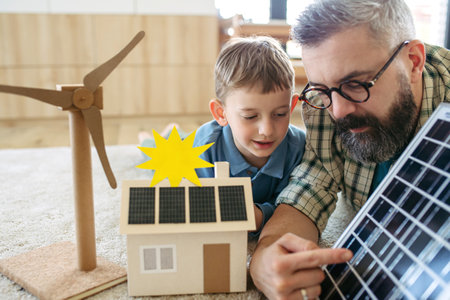 Father explaining renewable energy, solar power and teaching about sustainable lifestyle his young son. Playing with model of house with solar panels.の写真素材