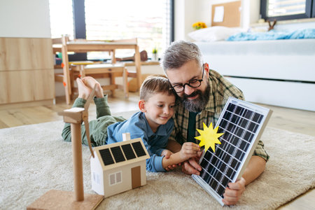 Father explaining renewable energy, solar power and teaching about sustainable lifestyle his young son. Playing with model of house with solar panels.の写真素材