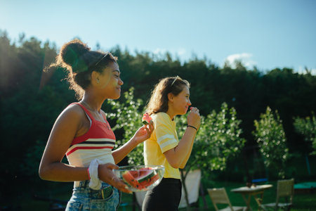 Young teenager girls friends outdoors in garden, eating watermelon.