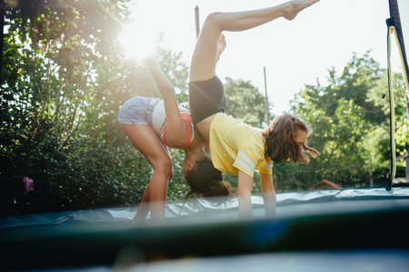 Teenage girls friends outdoors in garden, doing exercise on trampoline, having fun, jumping.の写真素材