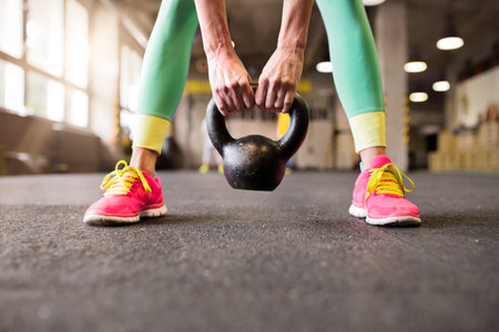 Sport woman performing kettlebell swing, holding kettlebell in hands, close up. Routine workout for woman's physical and mental health.の写真素材