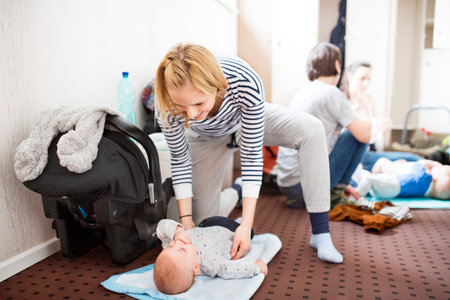 Mother changing baby after during group exercise class. Moms staying active, working out with babies in gym, bonding.の写真素材