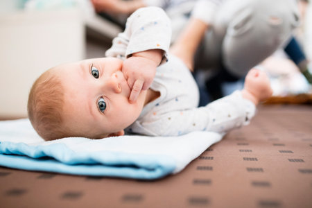 Portrait of cute little baby with fingers in mouth, looking at camera.