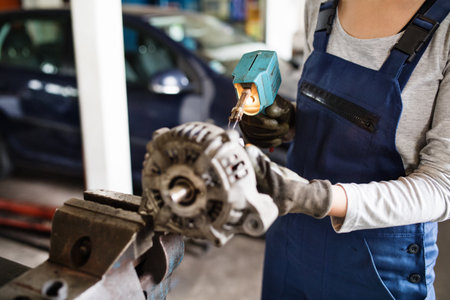 Female auto mechanic repairing, maintaining a car. Beautiful woman working in a garage, wearing blue coveralls. Female automotive service technican.の写真素材