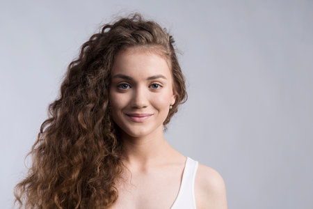 Portrait of a gorgeous teenage girl with curly hair. Studio shot, white background with copy spaceの写真素材