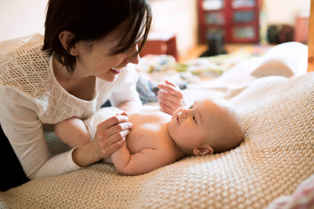Mother playing with small baby lying on bed. Unconditional paternal love, mothers Day concept.の写真素材