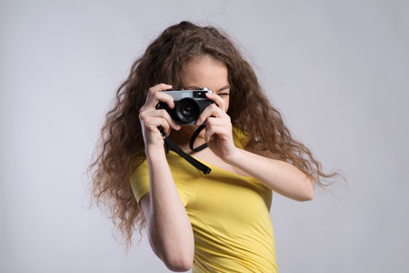 Portrait of a gorgeous teenage girl with curly hair holding camera. Studio shot, white background with copy spaceの写真素材