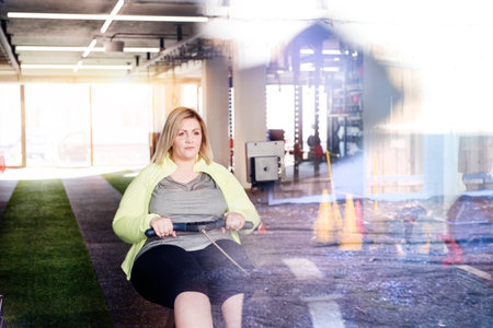 Overweight woman exercising on rowing machine. Routine workout for physical and mental health