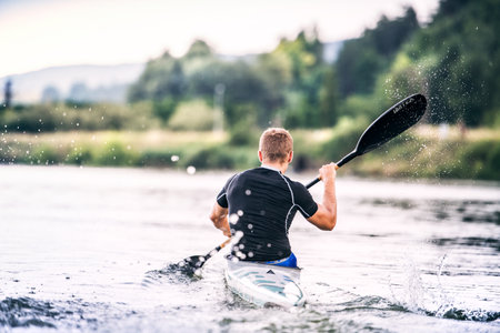 Canoeist man sitting in canoe paddling, in water. Concept of canoeing as dynamic and adventurous sport. Rear view, sportman looking at water surface, paddlingの写真素材